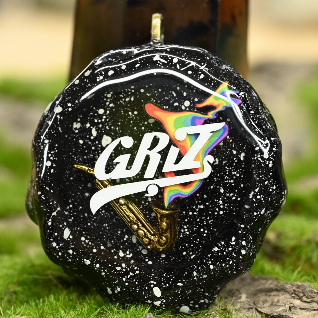 Hollow pinecone necklace pendant painted with a starry black sky, and overlaid with a metal mini saxophone, rainbow emerging from the saxophone, and a GRiZ logo all sealed in clear epoxy.