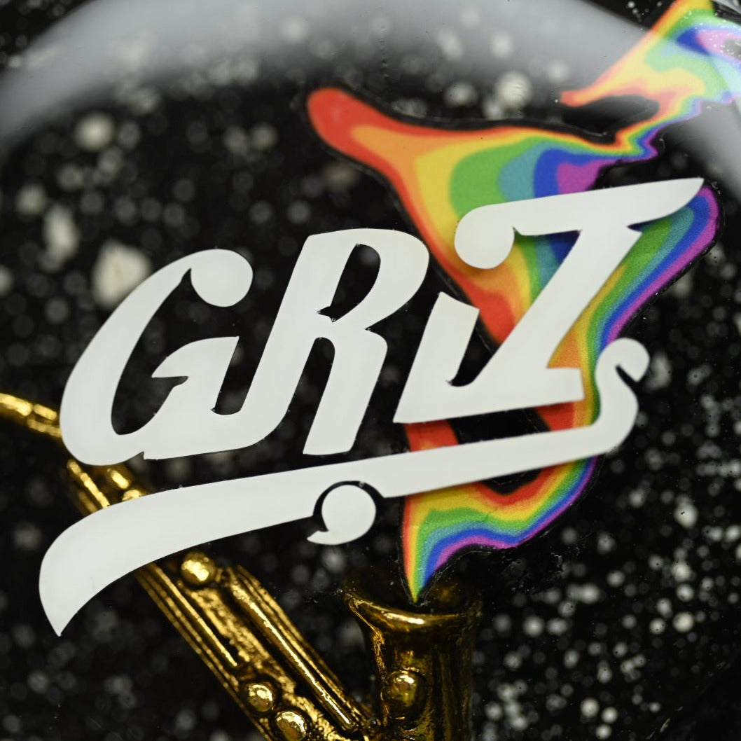 Closeup of the saxophone, rainbow, and GRiZ logo in the pinecone pendant.